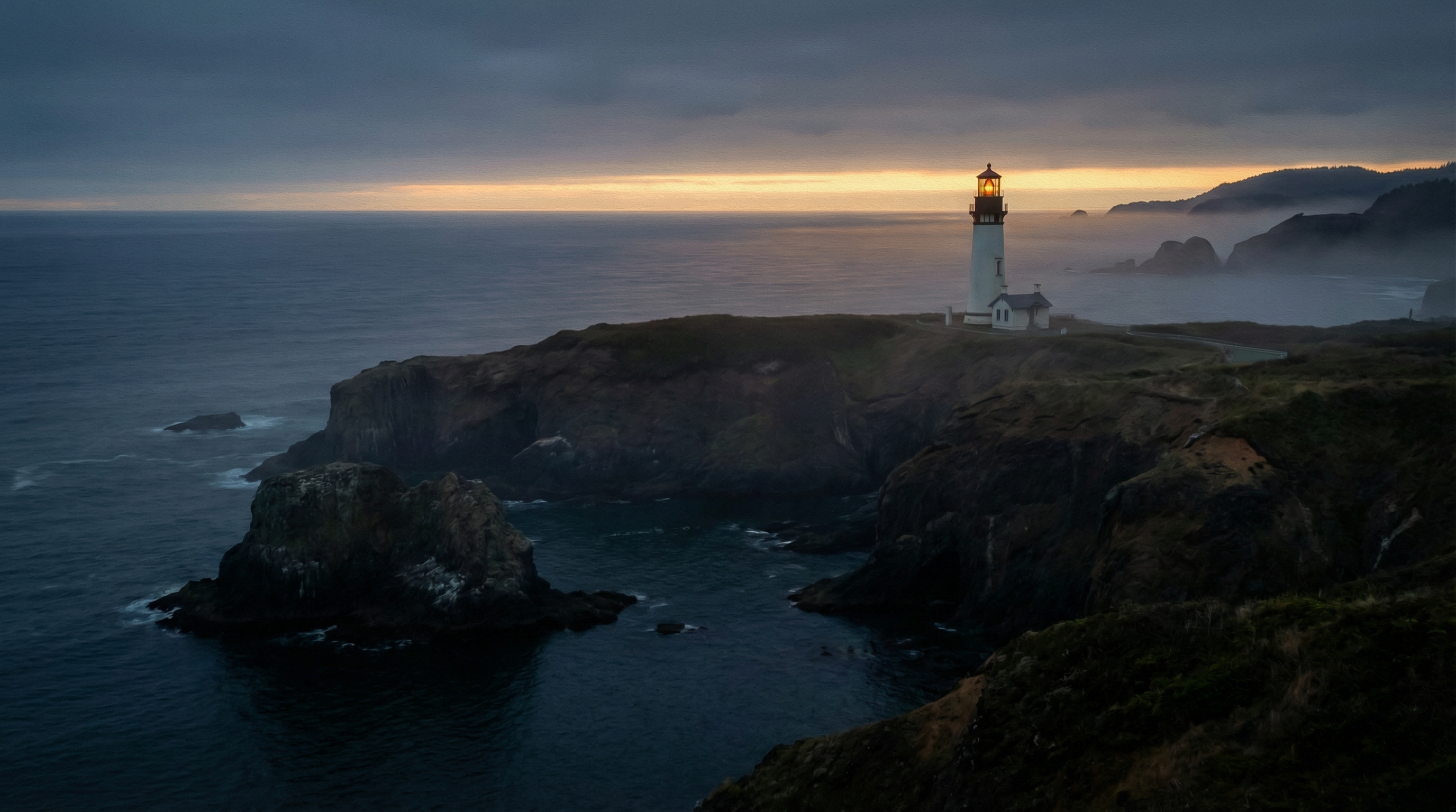 Yaquina Head Lighthouse standing on a dark basalt headland 162 feet above the Pacific Ocean at dusk, its amber light just beginning to glow